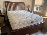 Photo of the complete bed setup showing the wooden slatted curved headboard, mattress, and part of boxspring underneath