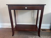 Front view of small wooden side desk showing drawer and open lower shelf, dark wood finish with scratches.