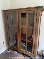 Photo of a tall wooden glass cabinet with two front doors, each with two vertical glass panels. Cabinet shows signs of wear and one glass panel is missing or broken.