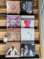 Photo showing eight vinyl records arranged in two columns. Covers include Elvis Presley in Concert, David Ruffin, Phoebe Snow, and several compilation albums. Records are in jackets/sleeves, some wrapped in plastic.