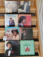 Collection of eight vinyl records arranged on wooden slats showing album covers, mostly featuring Enrico Macias.