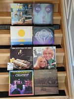 Photo of eight vinyl records arranged on a wooden bench, showing diverse album artwork and artists.