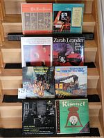 Set of eight vinyl record covers displayed on wooden steps. Records include classical and theatrical music albums with various artists and composers.