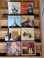 Seven vinyl records arranged on wooden display steps, showing cover art for various classical and Spanish guitar music albums by artists including Carlos Montoya, Laurindo Almeida, Al Caiola.