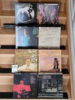 Eight vinyl records displayed on wooden stairs, showing front covers including Outlaws, Neil Young, John Gary, Michael Martin Murphey, Elton John, and Crazy Horse