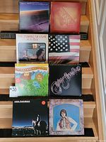 Eight vinyl records stacked in two rows on wooden stairs showing The Beach Boys Endless Summer, Captain & Tenille Greatest Hits, Ian Thomas albums, among others.