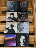 Photo of eight vinyl records arranged in two rows of four on a wooden stand. Albums include Ohio Players 'Stand Back' (2 copies), Catherine Johnson, Flanders & Swann, Lotte Lehmann, Laura Fygi, and others. All records are in jackets/sleeves.