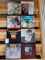 Front view of 8 vinyl records arranged in two rows on wooden steps, showing front covers including The Animals, Glenn Gould, Rick Wakeman, Saga, Bach and Copland albums.