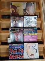 Photo depicting eight vinyl records arranged in two rows on wooden surface, showing all cover arts clearly