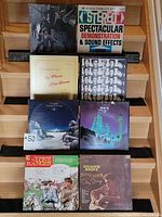 Photo showing 8 vinyl records arranged on wooden stairs, covers visible including Steppenwolf, Stereo Spectacular Demonstration, No Place At Home, and others with space-themed and country covers.