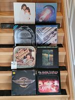Seven vinyl records arranged in two rows on wooden stairs. Visible albums by Ultravox, Pat Benatar, Arlo Guthrie, The Doobie Brothers, and compilations.