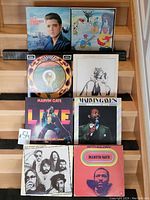 Eight vinyl records arranged in two rows on a wooden surface: Elvis Presley Christmas album, an album with eclectic illustration, Marvin Gaye live and greatest hits albums, The Doobie Brothers album, and a Marvin Gaye red-toned portrait album.