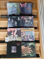 Photo showing eight vinyl record covers arranged on stairs, featuring Santana, Kiss, Eddy Grant, Sweet, Linda Ronstadt, and Decoyto.