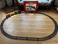 Oval shaped black track with battery operated train set assembled, locomotive and three cars.
