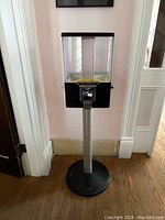 Front and side views of four-sided candy dispenser mounted on metal stand showing coin slots and compartments