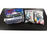 Box and components laid out: kit box with artwork of 1966 Shelby GT350H along with grouped plastic bags containing model parts, paint bottles, brushes, and cement.