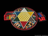 Full view of the round vintage 1970s reversible tin Chinese Checkers board with colorful sections and illustrations, showing red and black sliding trays loaded with colored marbles.