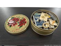 Photo shows a round decorative tin with a floral design lid containing various vintage buttons, some on original cards and some loose.