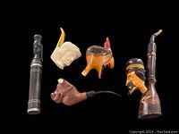 Four vintage carved pipes including a meerschaum carved face pipe, a bull head pipe, a carved wooden head pipe with a man's face, and a dagger-shaped pipe with sheath.