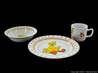 Photo showing the full 3-piece porcelain children's dish set including the Big Bird plate, bowl and mug against a black background.
