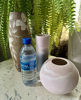 Photo showing three different Mid-Century Modern style sandstone vases of varying shapes and sizes beside a water bottle for size reference.