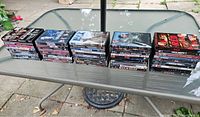 Four stacks of assorted DVDs totaling 50, showing various movie titles and typical DVD packaging, set on a glass table outside.