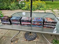Overview photo showing all 50 DVDs stacked in neat rows on a glass table outdoors, visible are multiple DVD cases with diverse titles.