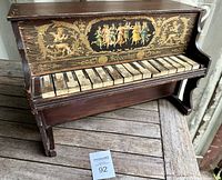Full view of antique Schoenhut child's piano showing front panel with decorative figures and wooden keys, worn and chipped.