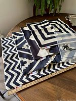 Four black and cream geometric patterned cushion covers laid out on a wooden table with a measuring tape showing 16 inches, each cover with different geometric pattern