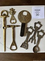 Photo showing all seven brass bottle openers on a flat surface with a note.
