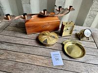 Lot overview showing all six items on a wooden surface: brass three-arm candleholder, cedar wood box, brass clock, brass thermometer, brass covered dish, and 'Small Change' tray.
