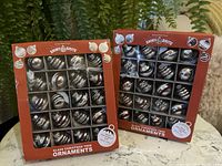 Two unopened boxes of Shiny Brite glass Christmas tree ornaments with red packaging showing ornaments inside with glitter stripes.