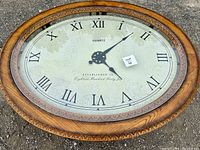Close-up photo of the clock face embedded under the glass top showing Roman numerals and decorative clock hands with some age wear.