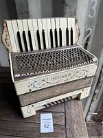 Front view of vintage Hohner accordion showing piano keyboard style keys, grille, and body with blue floral decoration and wear.