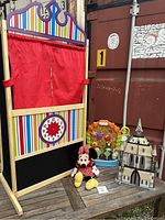 Full view of Melissa & Doug Deluxe Puppet Theatre, Minnie Mouse plush, doll house castle, and Little Tikes play centre on wooden surface.