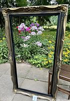 Front view of the large vintage rectangular frame standing outdoors with garden background showing full frame details including ornate scroll and floral design with black and gold coloring.