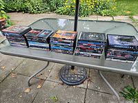 Photo of multiple stacks of DVD cases laid out on an outdoor table, showing the variety and quantity of DVDs included in the lot.