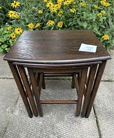 Front angled view of three stacked dark wood nesting tables showing their size and shape relationship with a background of yellow flowers.