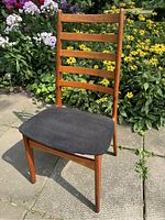 Front view showing teak wood frame with ladder back and black fabric seat upholstery.