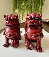Front view of pair of red resin Chinese Foo Fu Dogs showing detailed facial features, collars and paws with objects.