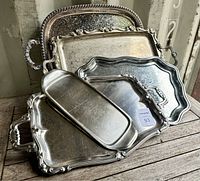 Five silverplated rectangular trays stacked, each with decorative edges and handles showing surface wear and scratches
