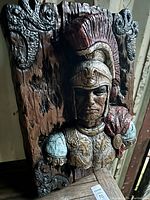Front view of the Roman warrior resin wall sculpture, showing the bust in detailed armor against a wood-like carved background.
