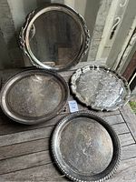 All four round silverplated trays shown together on wooden surface, visible tarnishing and wear noted.