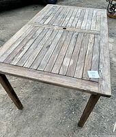 Overall view of weathered teak patio table showing rectangular shape, slatted top, and central umbrella hole.