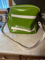 Front view of vintage bright green Alitalia flight crew travel bag with white piping and shoulder strap on countertop.