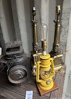 Lot of 4 lamps including matching MCM brass lamps, yellow railroad lamp on wooden base with Edison bulb, and antique railroad lantern cover showing wear.