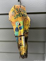 Side angled photo of hand-painted wooden bark margarita sign showing parrot, clock and textual elements