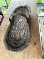 Top view of a large, oval, handwoven basket with a single sturdy handle, placed on a wooden surface.