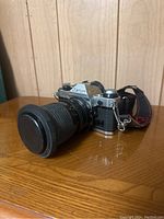 Side angle showing Canon film camera with attached black zoom lens and lens cap, placed on wooden surface.