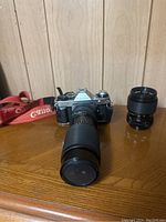 Front view of Canon camera with long zoom lens attached and second shorter lens beside it on wooden surface.